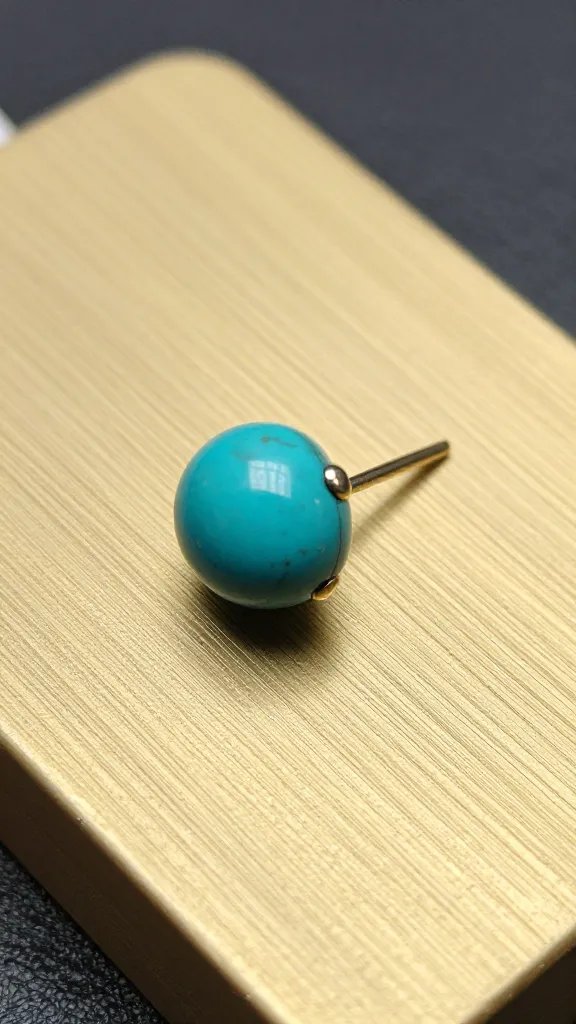small turquoise stud earring on brushed brass display, closeup